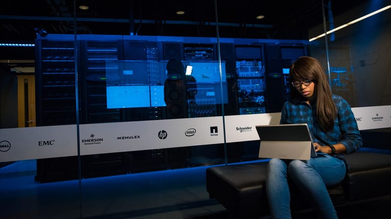 Woman using a laptop in a server room, showcasing modern technology and work environment.