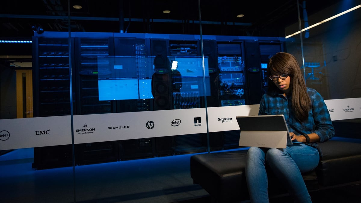 Woman using a laptop in a server room, showcasing modern technology and work environment.