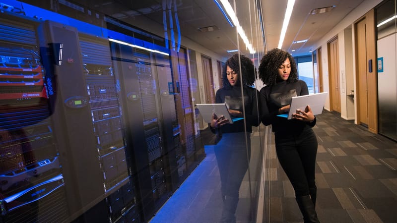 A woman using a laptop navigating a contemporary data center with mirrored servers.
