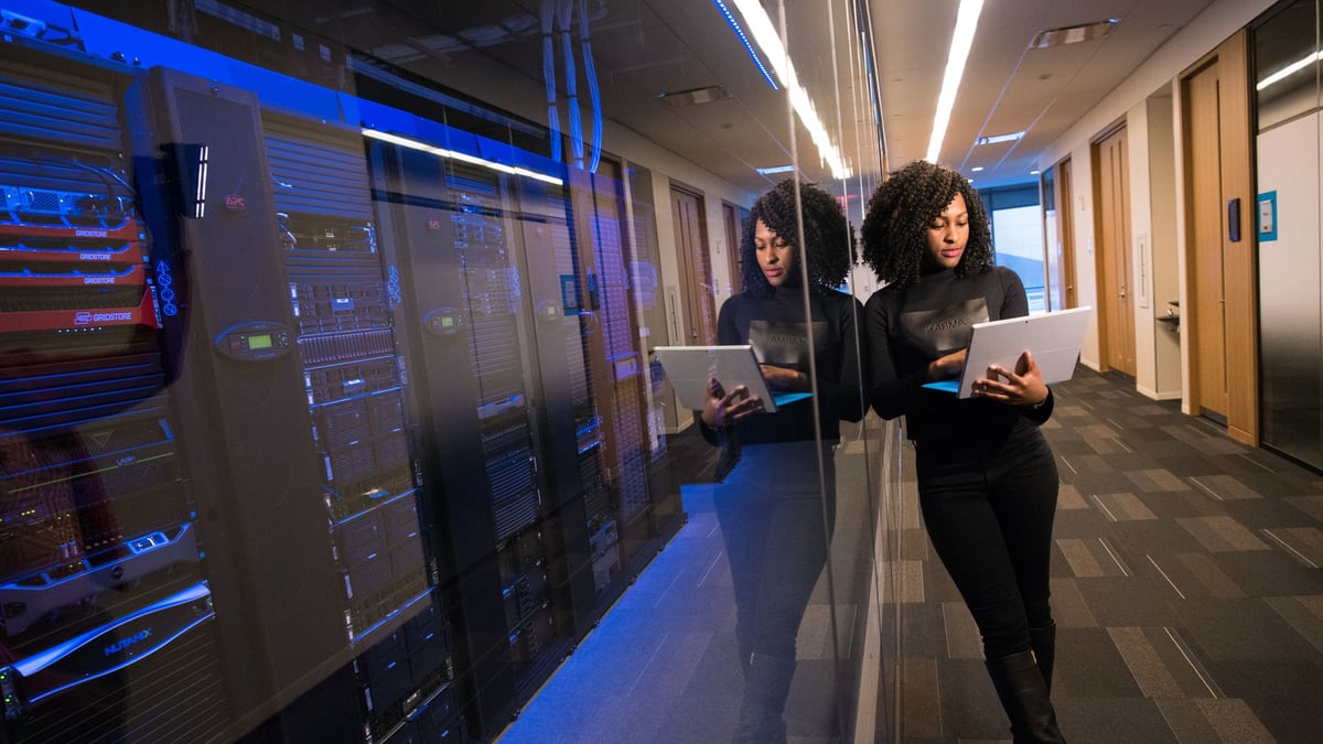 A woman using a laptop navigating a contemporary data center with mirrored servers.