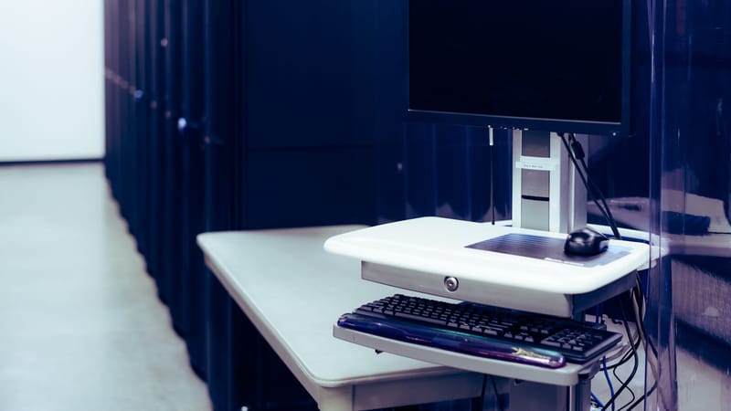 Contemporary computer with black screen placed on stand near row of server steel racks in data center