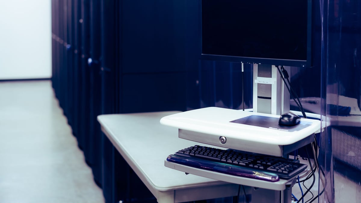 Contemporary computer with black screen placed on stand near row of server steel racks in data center