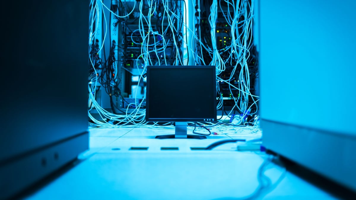 A complex network of cables in a data center with a monitor in the foreground.